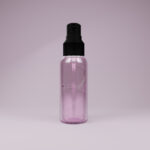 A transparent pink spray bottle with a black nozzle and cap stands upright against a soft, neutral background. The bottle contains a visible spiral tube inside, which extends from the bottom to the nozzle. The lighting is soft and diffused, creating subtle reflections on the smooth plastic surface.